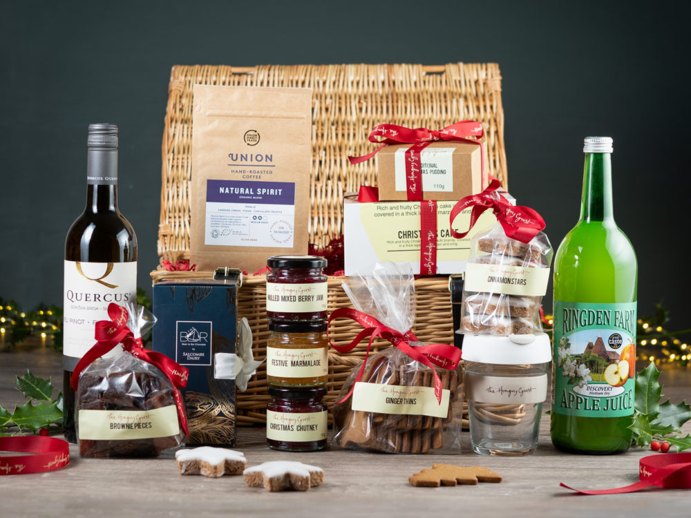 Wicker hamper including festive marmalade, chutney, jam, Christmas pudding and cake, ginger thins, cinnamon stars, brownie pieces, union coffee, Ringden apple juice, salcombe dairy chocolate bar library, bottle of red or white wine and a HG KeepCup.