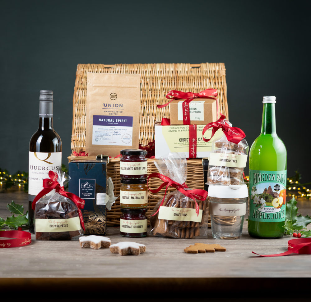 Wicker hamper including festive marmalade, chutney, jam, Christmas pudding and cake, ginger thins, cinnamon stars, brownie pieces, union coffee, Ringden apple juice, salcombe dairy chocolate bar library, bottle of red or white wine and a HG KeepCup.