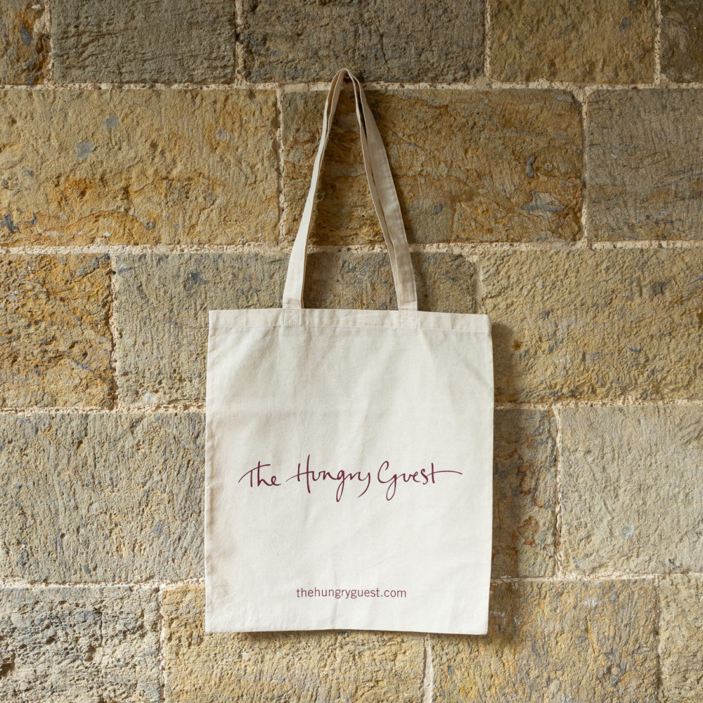 Hungry Guest canvas tote bag in cream hanging on a brick wall